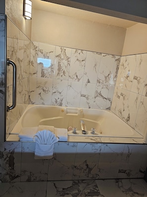 A spacious bathroom with a large bathtub, marble tiles, a handrail, and a towel rack.
