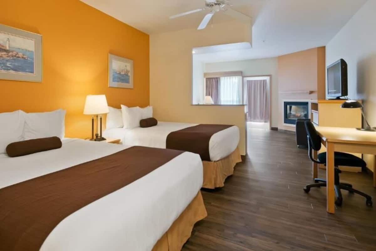 A hotel room with two beds, a desk, a chair, a television, and a fireplace.