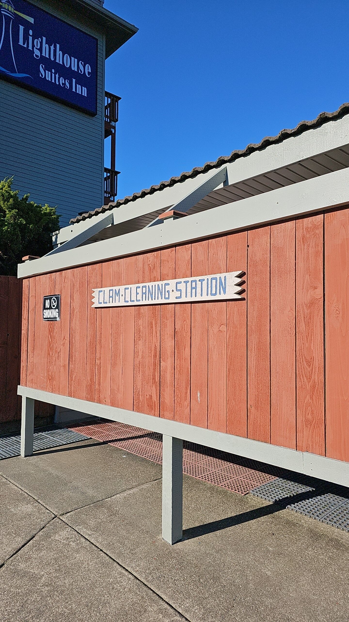A wooden structure labeled "CLAM CLEANING STATION" with a "NO SMOKING" sign, adjacent to a building with a sign reading "Lighthouse Suites Inn".