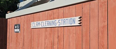 A wooden structure labeled "CLAM CLEANING STATION" with a "NO SMOKING" sign, adjacent to a building with a sign reading "Lighthouse Suites Inn".