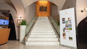 A modern hotel lobby with a marble staircase, a reception desk, and a large informational poster. - Phi Hotel Principe (Cuneo)