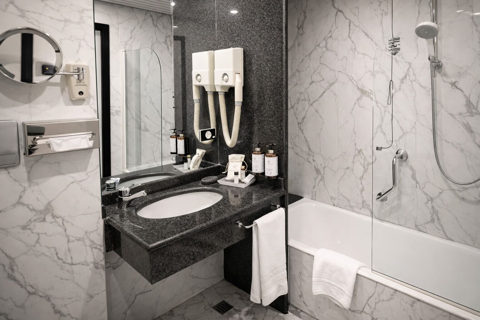 Un bagno moderno con un lavabo in marmo, uno specchio grande, un soffione doccia a mano e un porta asciugamani.