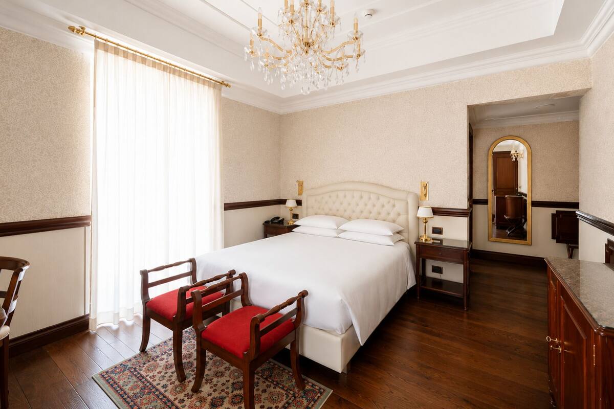 A hotel room with a large bed, a chandelier, a wooden desk, and a mirror.