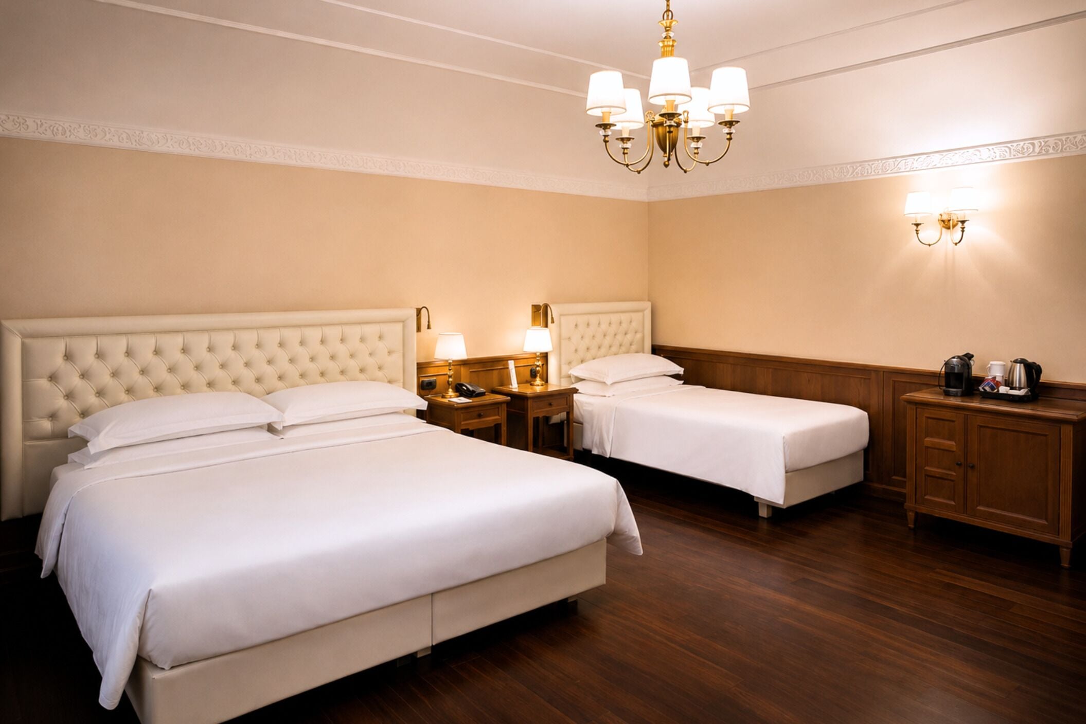 Une chambre d’hôtel avec deux lits, un lustre, des lampes de chevet, une table de chevet et une armoire en bois.