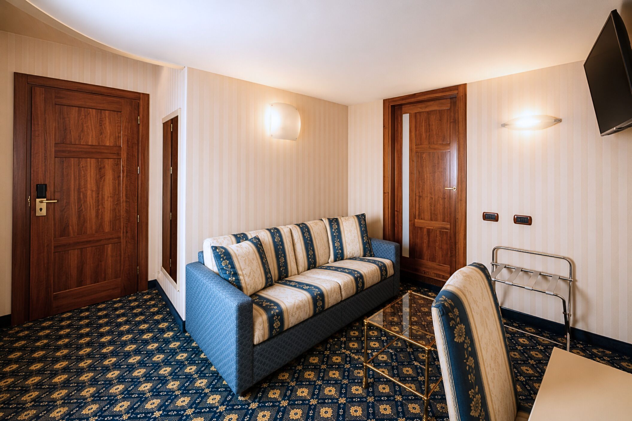Une pièce comprenant un canapé, un fauteuil, un téléviseur et un tapis à motifs.