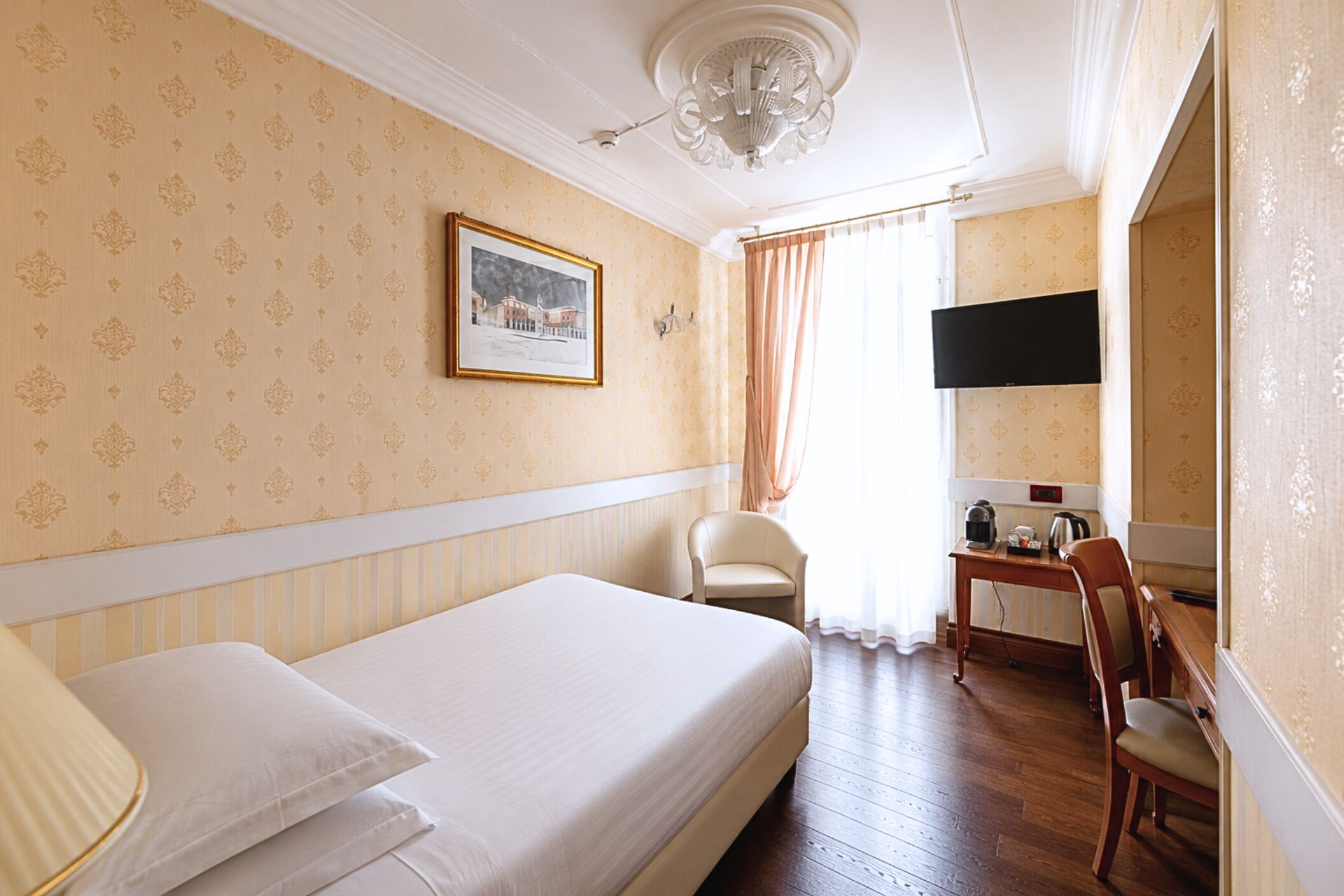 Habitación de hotel con cama, una silla, una mesa, televisor y un cuadro en la pared.