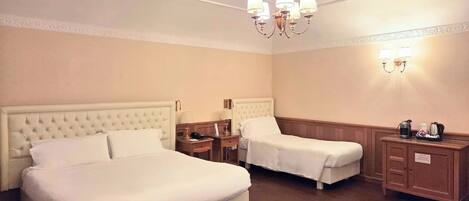 A hotel room with two beds, a chandelier, bedside lamps, a nightstand, and a cabinet with a coffee maker.