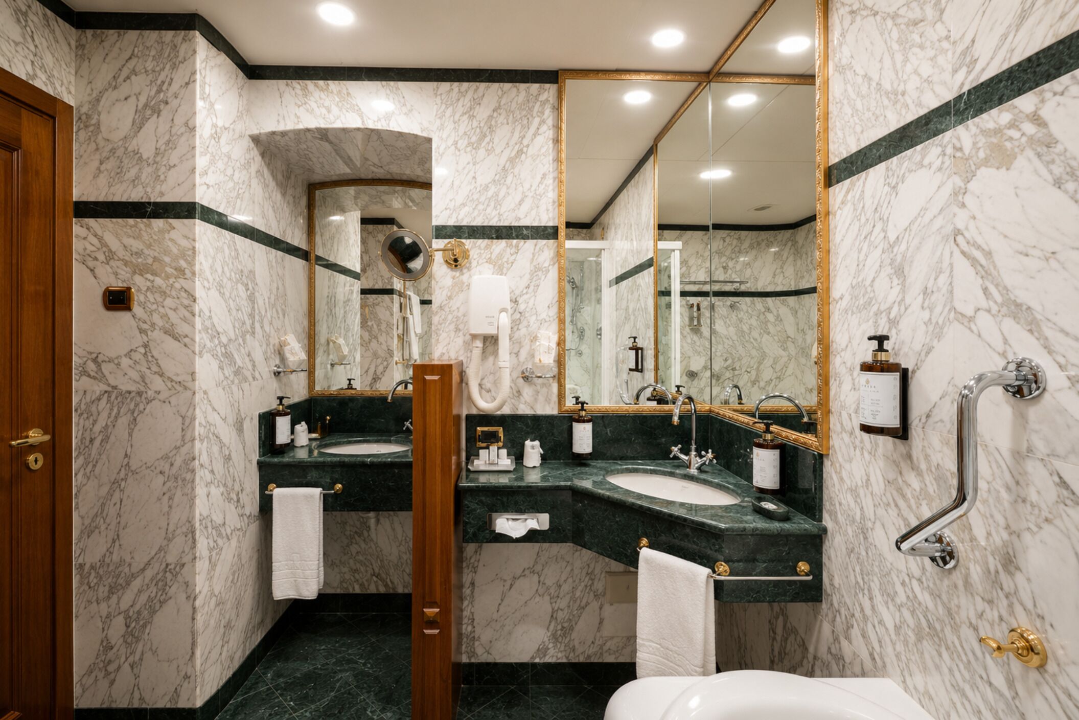 A marble bathroom with two sinks, a mirror, a toilet, and a shower.