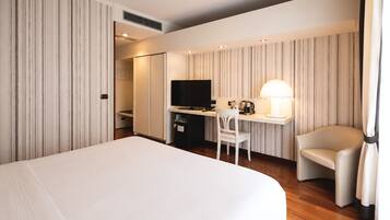 A hotel room with a large bed, a desk with a TV, a chair, and a lamp.