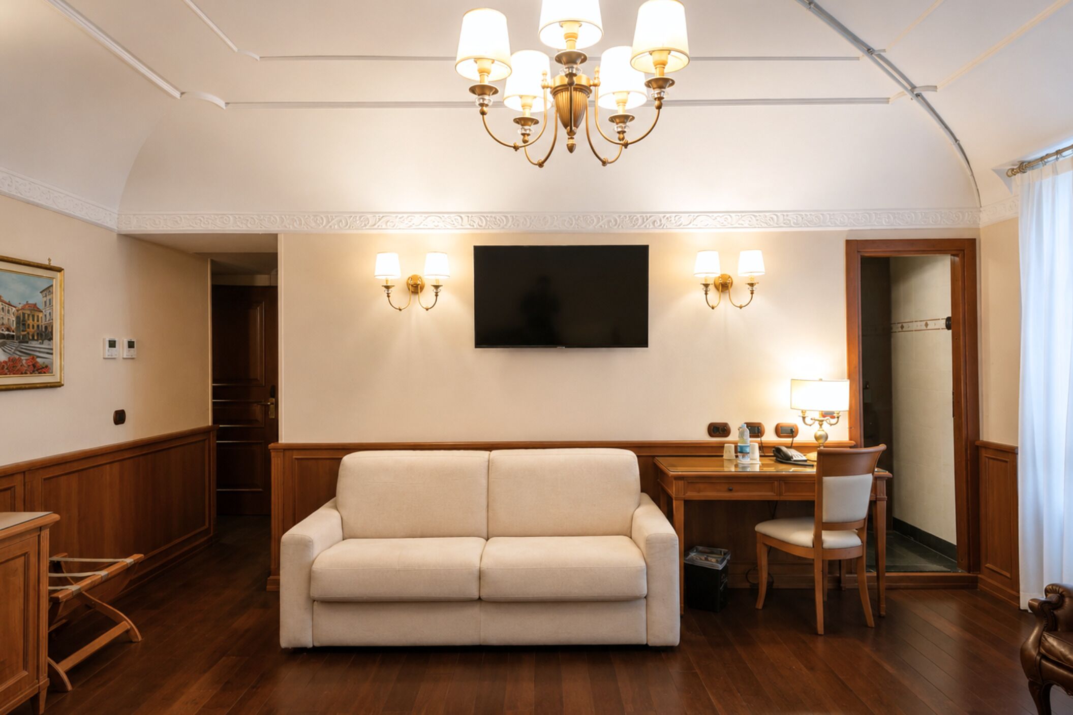Una habitación con sofá, escritorio, silla, televisor y lámparas de pared.