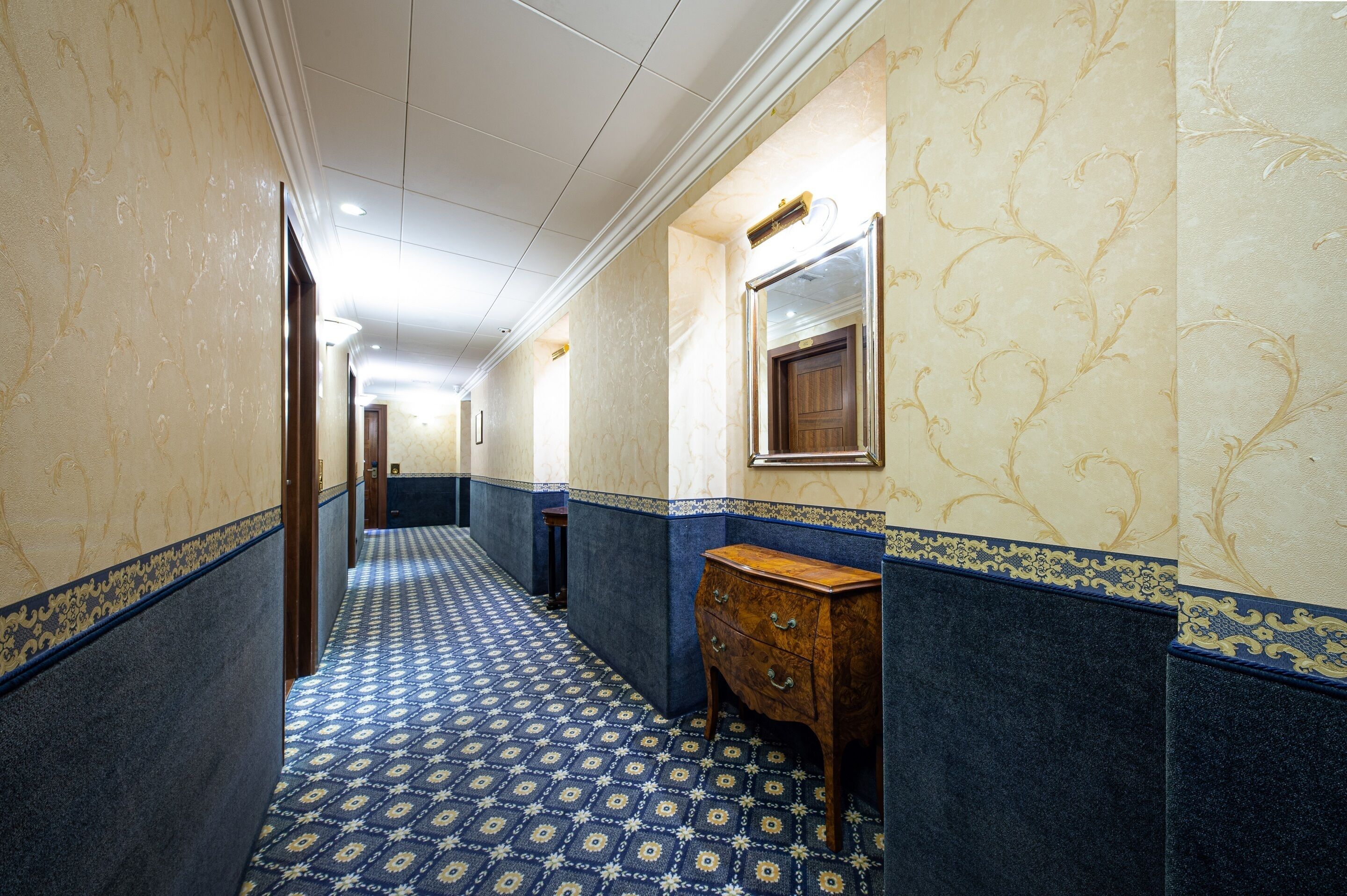 A hallway with patterned carpet, marble walls, and a wooden dresser.