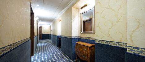 A hallway with patterned carpet, marble walls, and a wooden dresser.