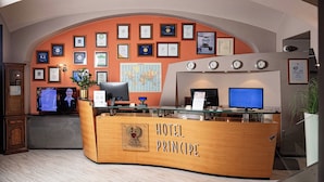 A hotel reception desk with a wooden counter, framed certificates on the wall, and a world map. - Phi Hotel Principe (Cuneo)