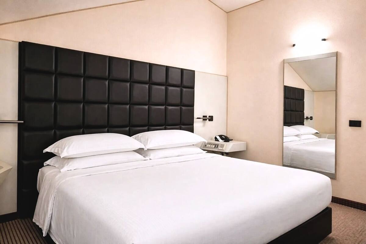 A hotel room with a large bed, a bedside telephone, and a mirror on the wall.