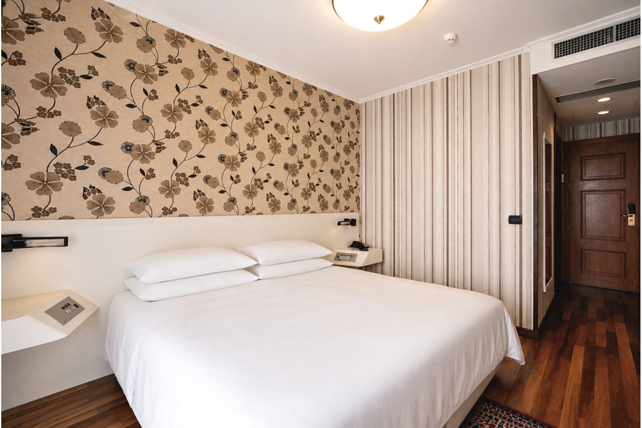 A hotel room with a large bed, a nightstand, a wall-mounted telephone, and a door leading to another room.