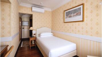 A hotel room with a bed, a nightstand, a lamp, a framed picture on the wall, and a door leading to another room.