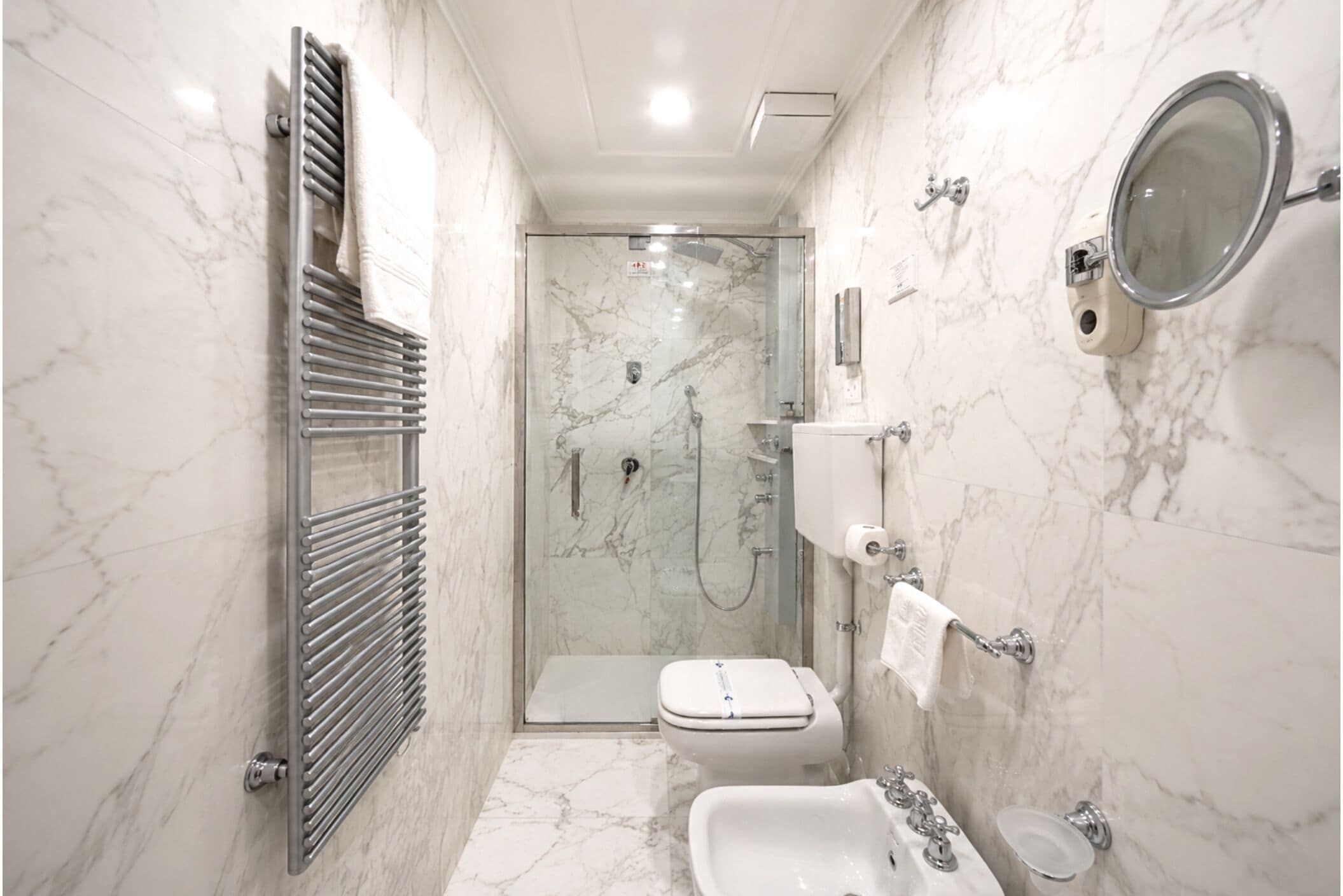 Een moderne badkamer met een douche met glazen wand, toilet, bidet, wastafel en spiegel.