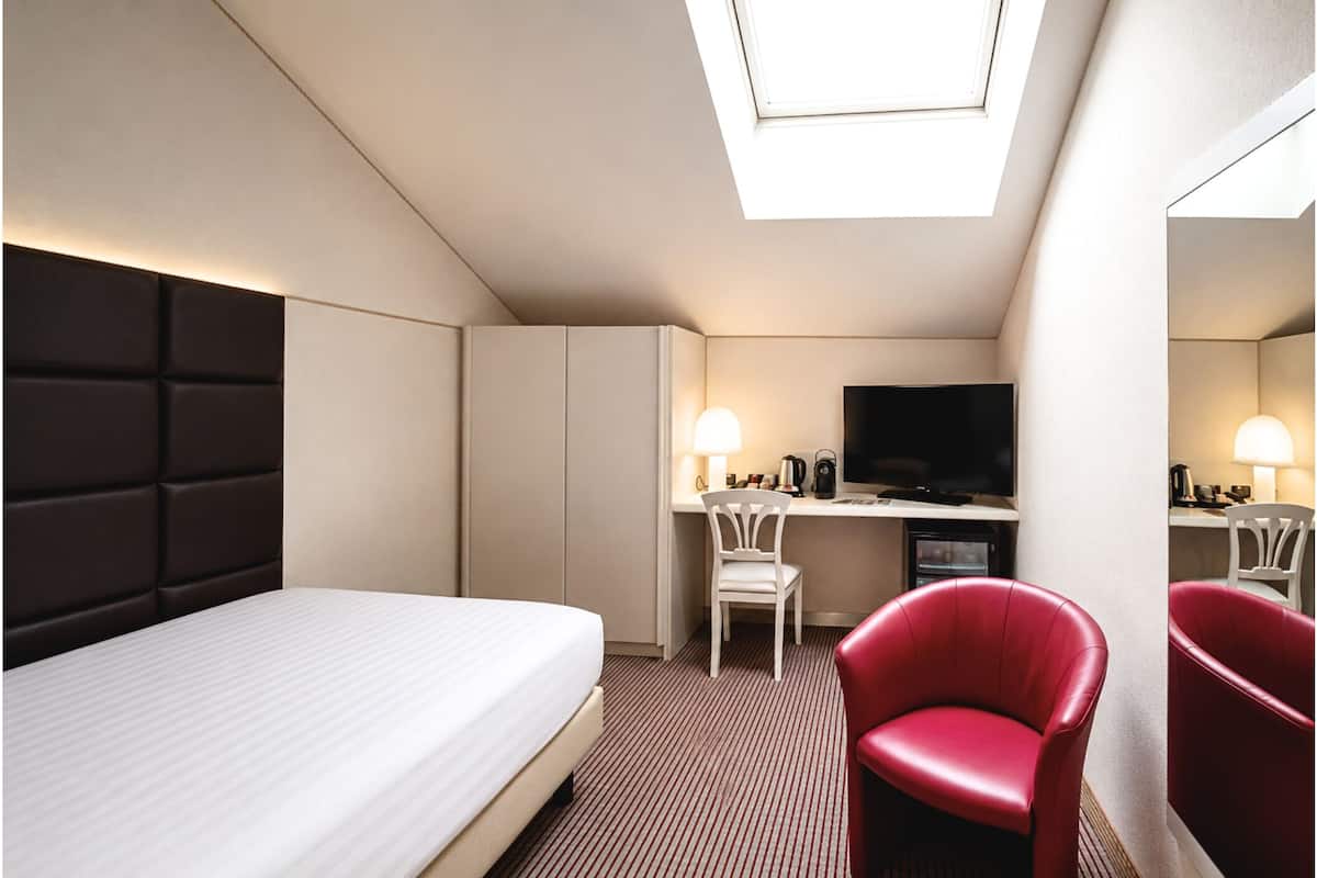 A hotel room with a bed, a desk with a TV, two chairs, and a skylight.
