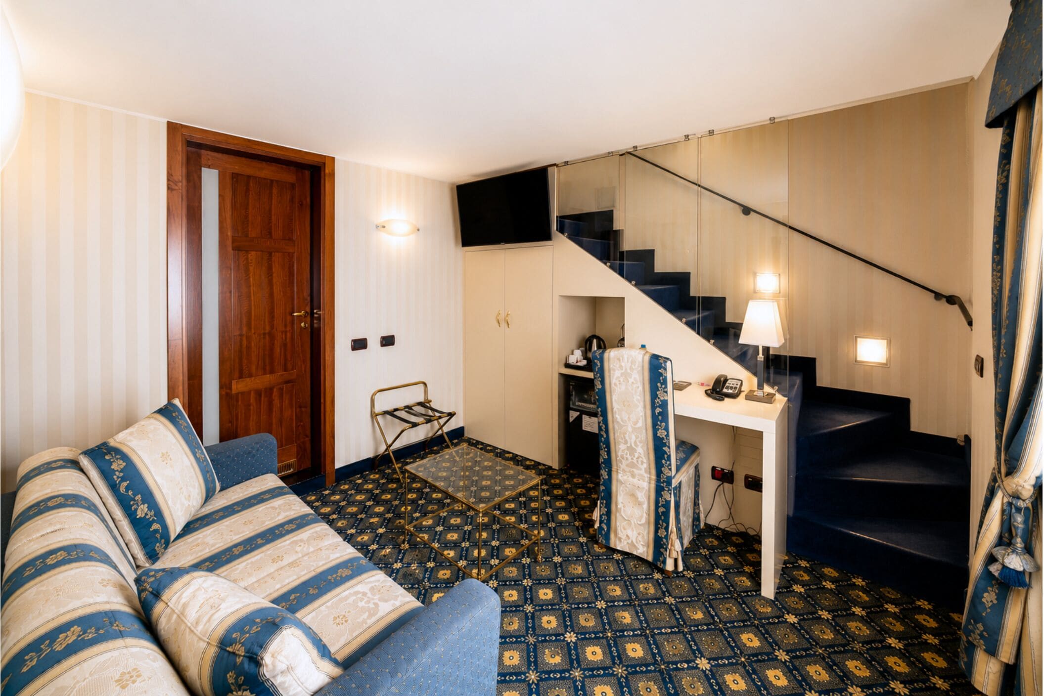 A room with a sofa, a small table, a chair, a staircase, and a door.