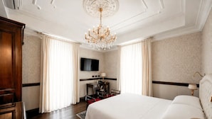 A hotel room with a large bed, a chandelier, a flat-screen TV, a desk, and a wardrobe. - Phi Hotel Principe (Cuneo)