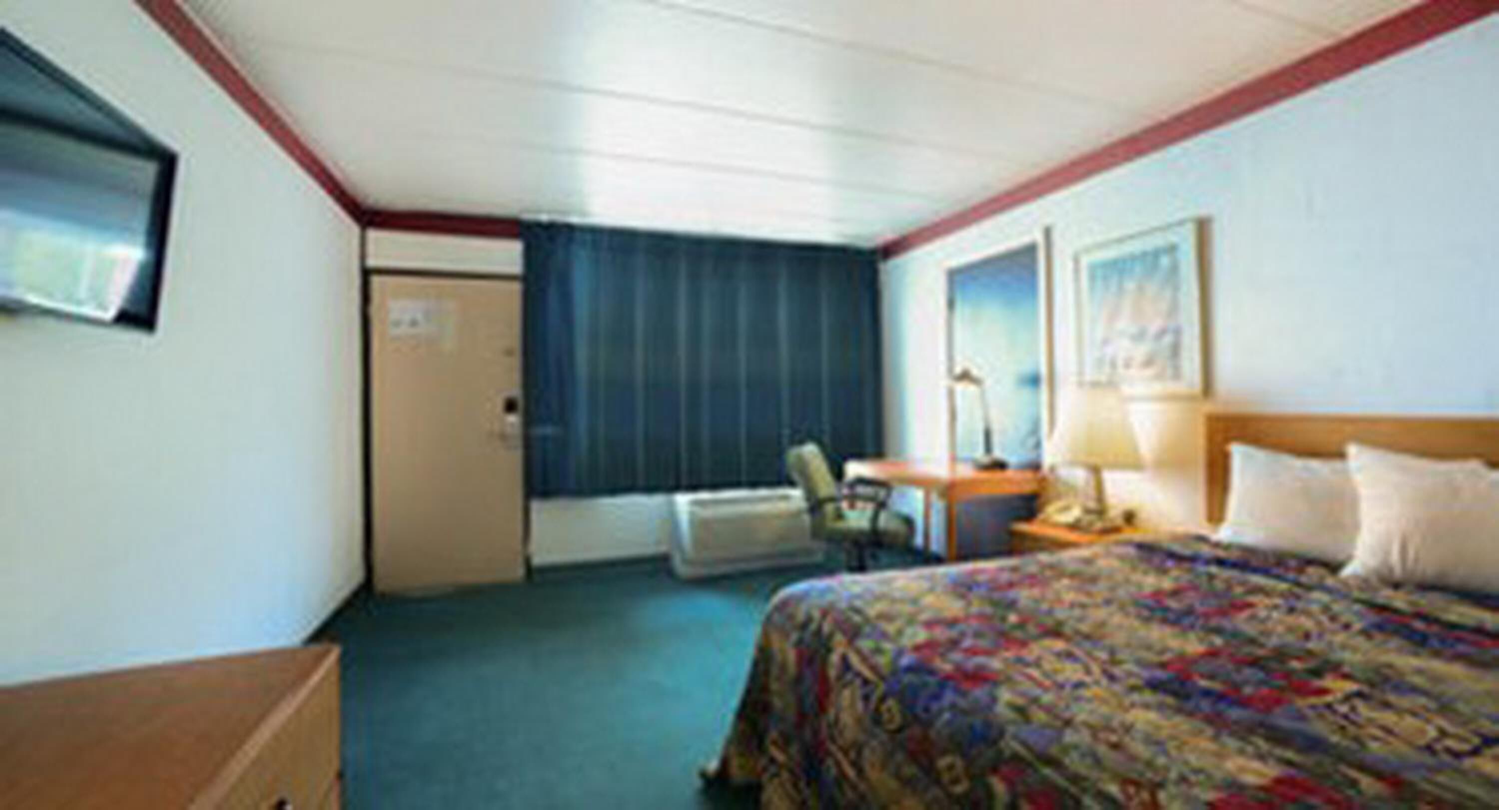 A hotel room with a bed, a desk, a chair, a window with curtains, and a door.