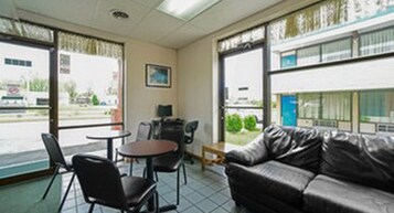 Quarto com sofá de couro, duas cadeiras, uma mesinha e janelas amplas com vista para o exterior.