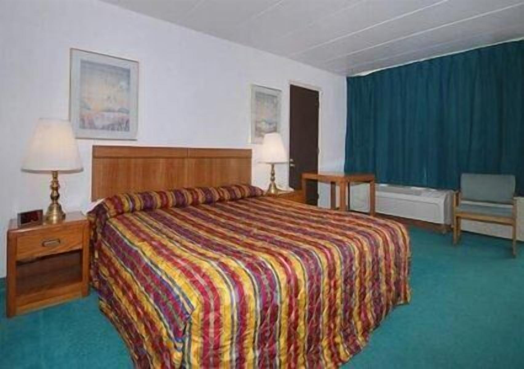 A hotel room with a wooden bed, two bedside tables with lamps, a chair, and a blue curtain.