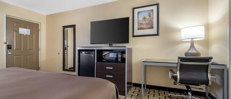 A hotel room with a bed, a desk, a chair, a television, a microwave, and a lamp.