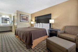 A hotel room with a bed, a chair, a nightstand, a lamp, a framed picture on the wall, and a bathroom with a mirror and sink. - Best Western Nursanickel Motel (Dalhart)