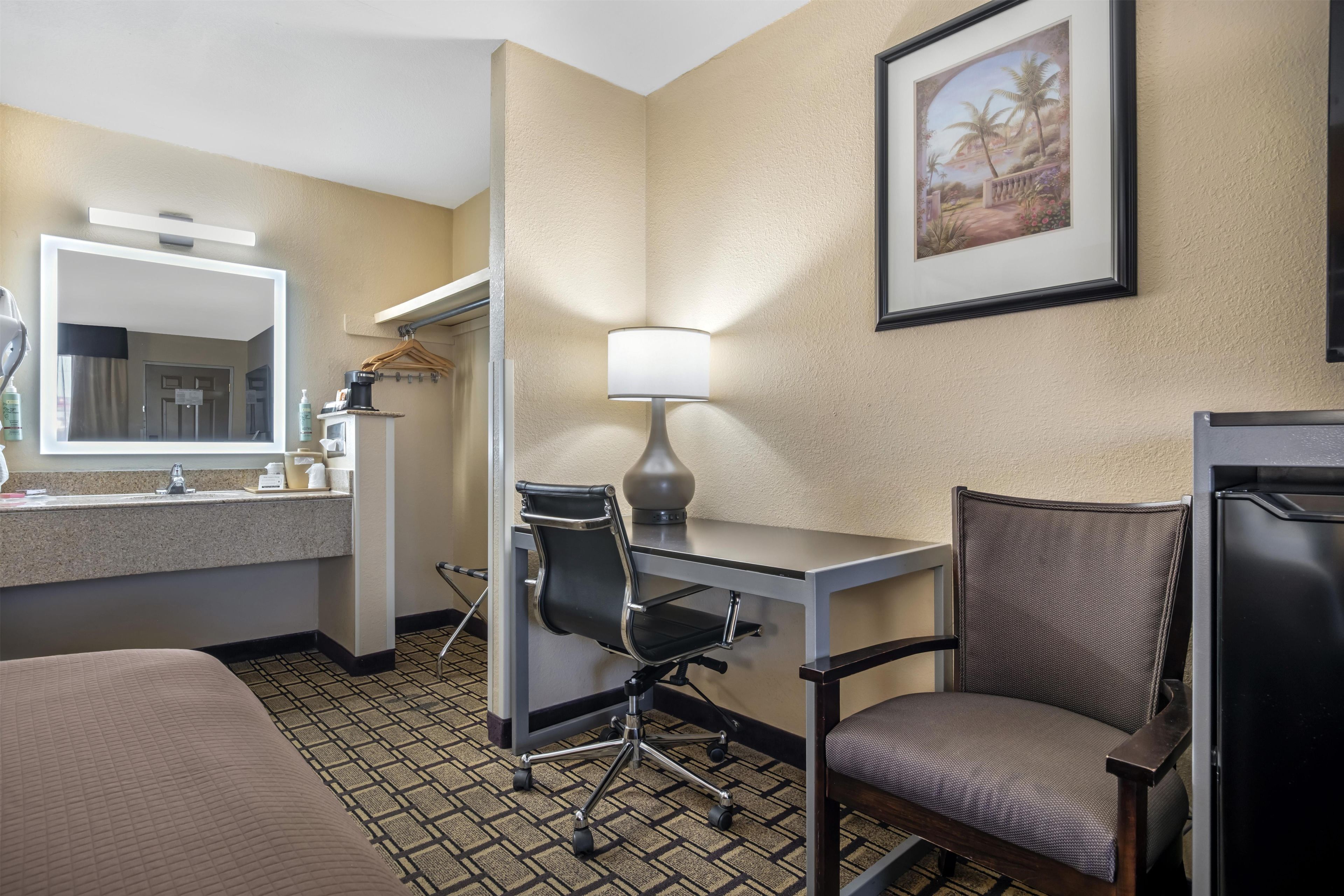 A hotel room with a desk, chair, bed, and a painting on the wall.