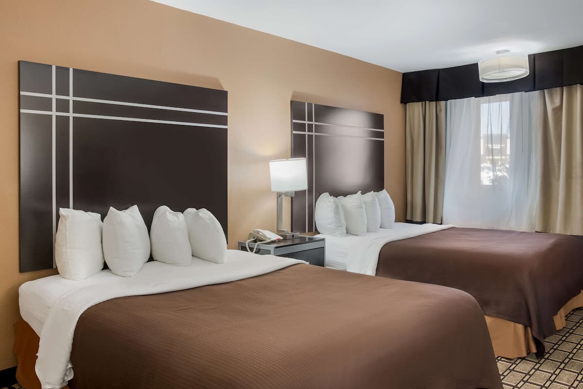Une chambre d’hôtel avec deux lits, une table de chevet avec une lampe et une grande fenêtre avec des rideaux.
