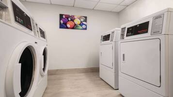 A laundry room with two front-loading washers and dryers, a wall-mounted control panel, and a colorful wall art piece.