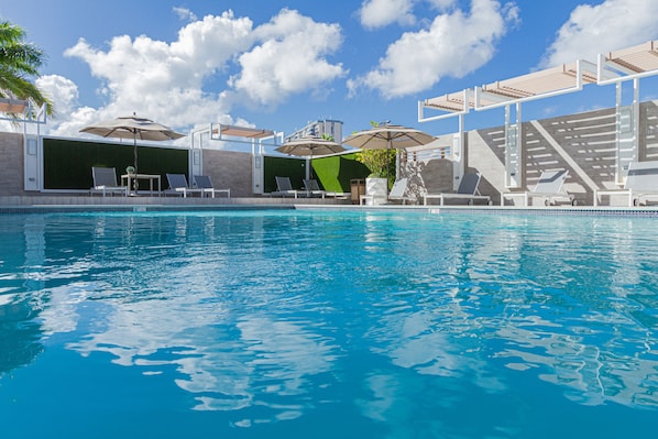 Una piscina al aire libre, sombrillas, sillones reclinables de piscina