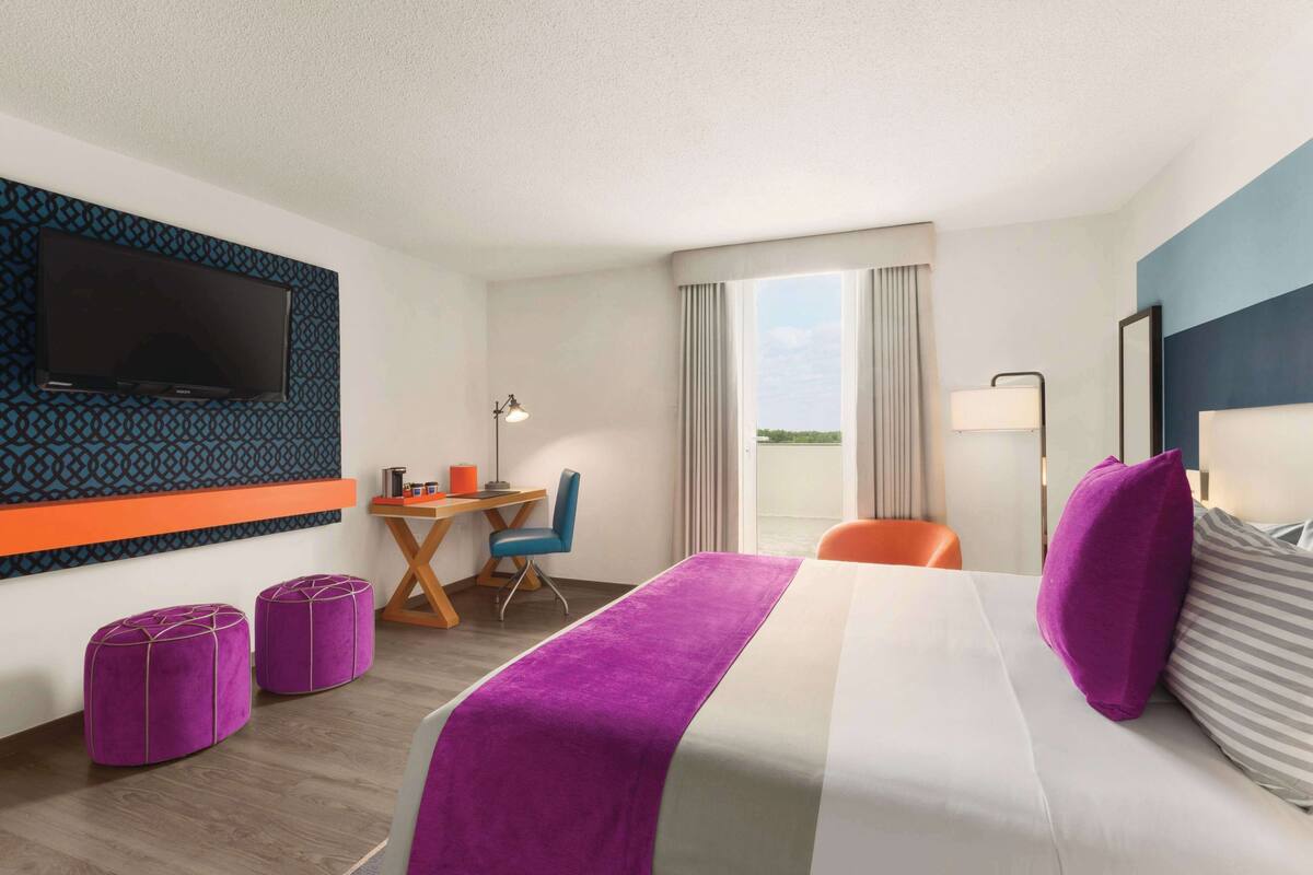 A hotel room with a bed, a desk, a chair, a TV, and a window with curtains.
