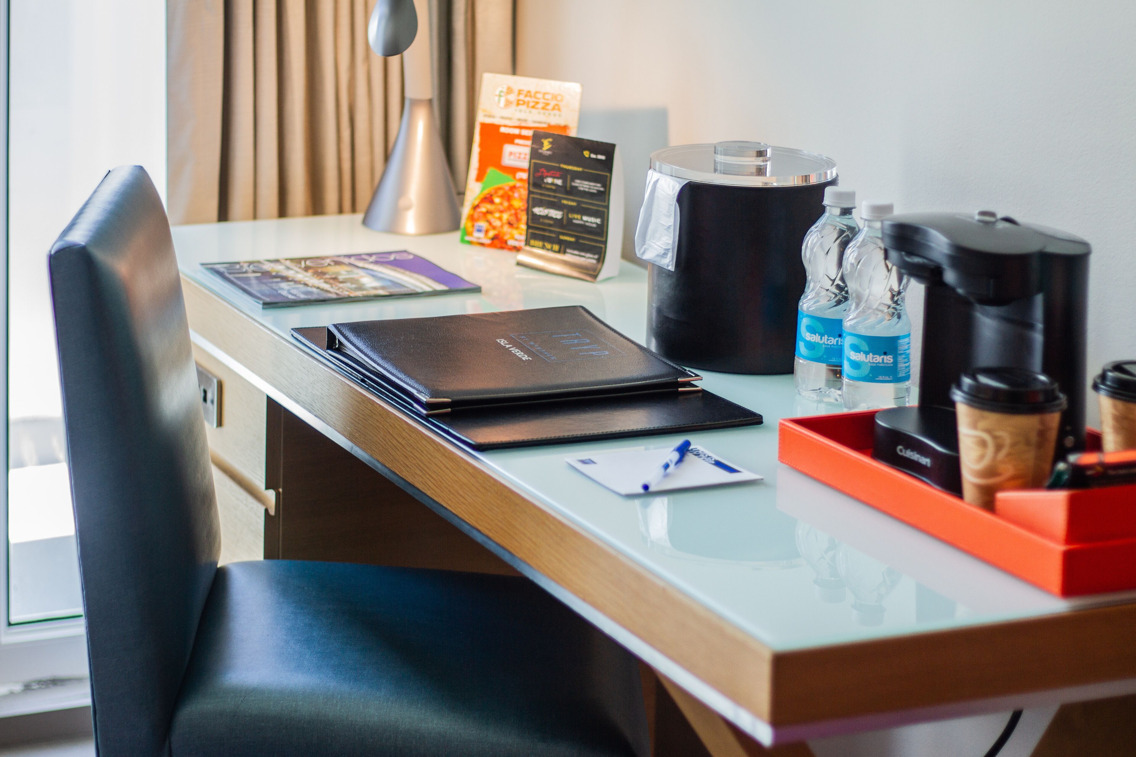 Un mostrador de hotel con un ordenador portátil, una caja de pizza, un fabricante de café y botellas de agua.