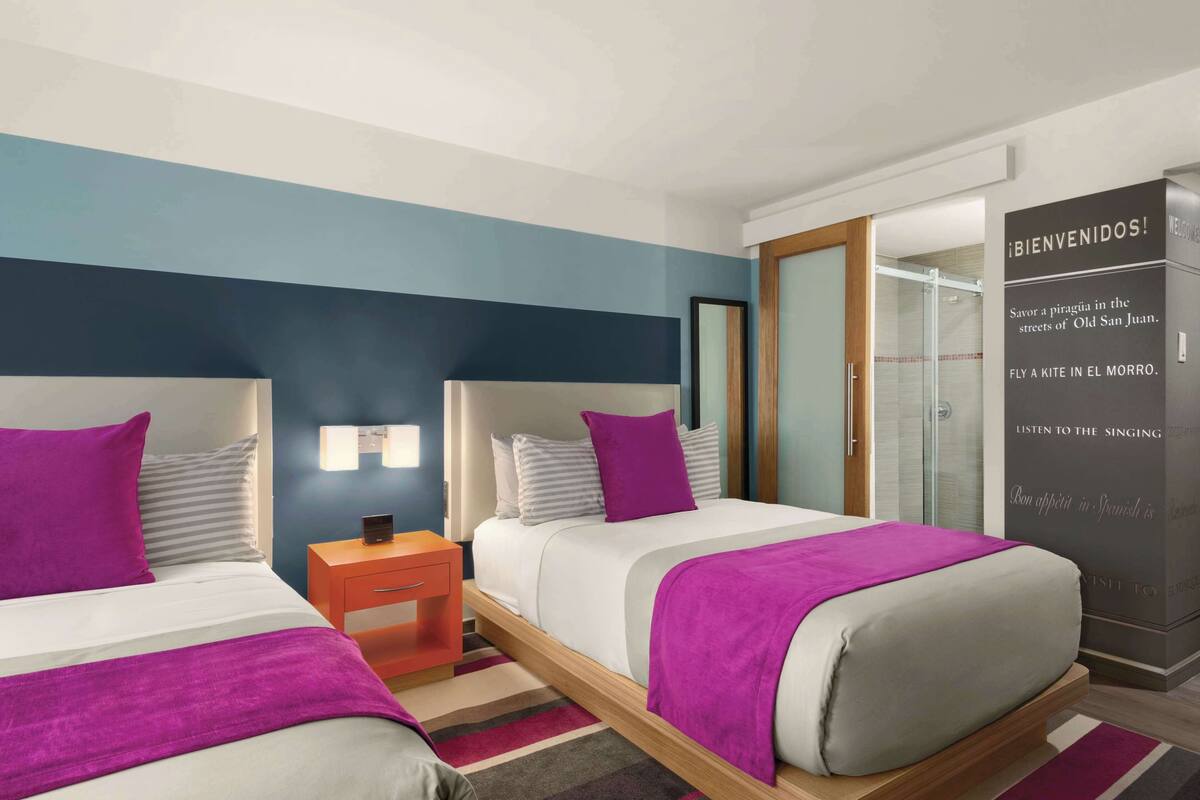 A hotel room with two beds, a nightstand, a mirror, and a wardrobe.