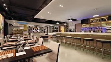A modern bar area with a long counter, bar stools, and a variety of bottles and glasses.