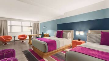 A modern hotel room with a large bed, two bedside tables, a desk, and two orange chairs.