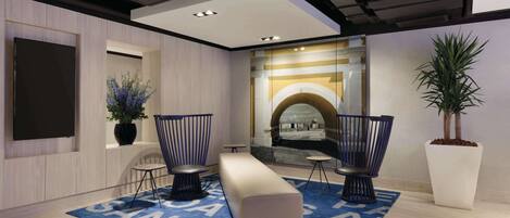 A modern lobby with a blue carpet, seating area, and a large potted plant.