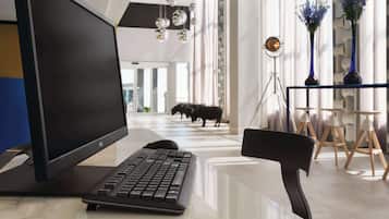 A modern office space with a large monitor, keyboard, and a black chair. There are decorative vases and a tripod lamp on a table.
