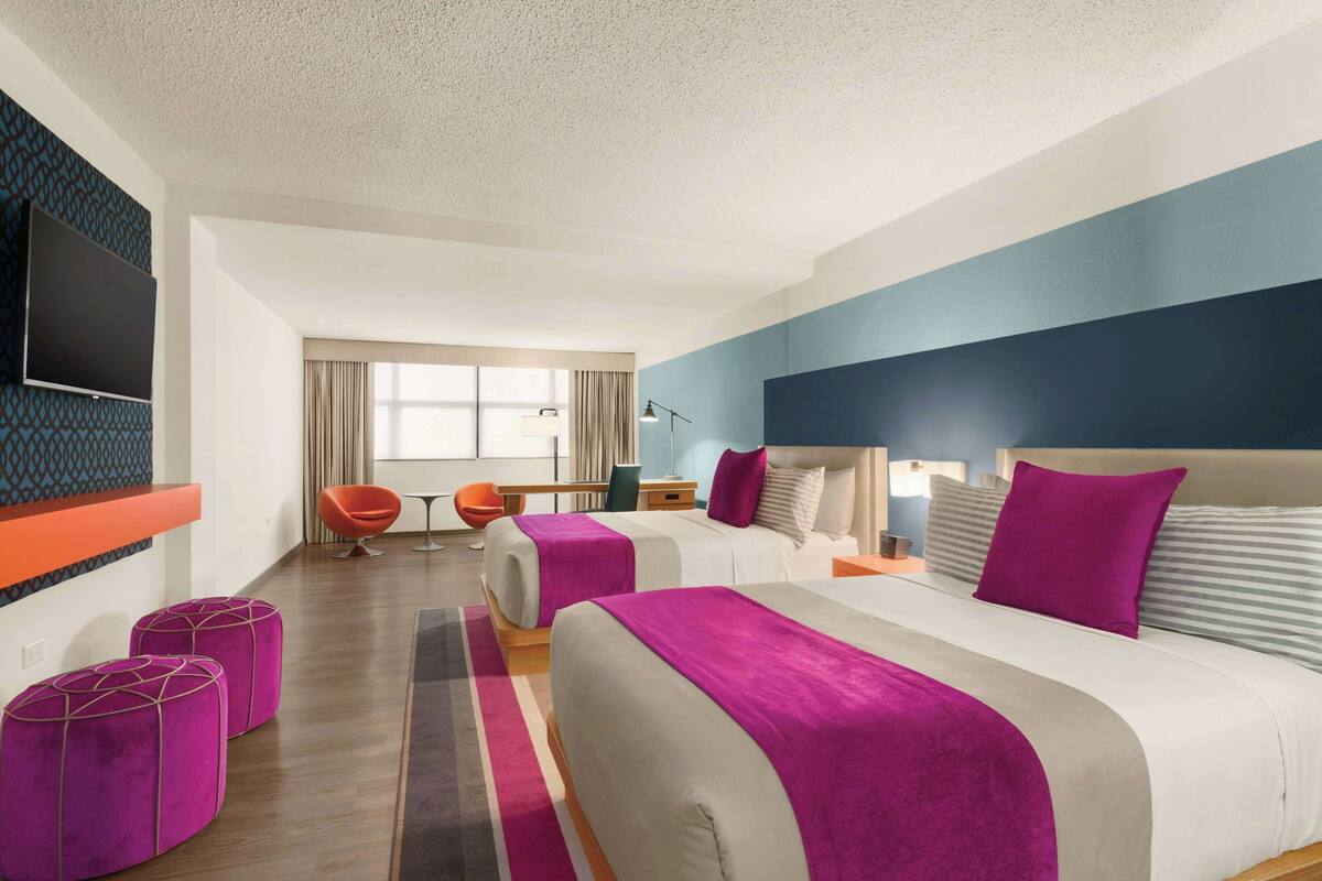 A hotel room with a large bed, two ottomans, a desk, a chair, and a TV mounted on the wall.