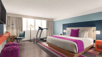 A hotel room with a bed, a desk, a treadmill, and ottomans.