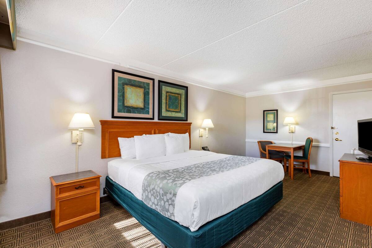 Una habitaci ón de hotel con una cama grande, dos mesitas de noche, un escritorio con una silla y un televisor sobre un aparador.