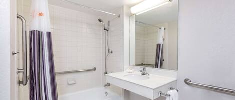 A bathroom with a white bathtub, a white sink with a mirror above it, and a shower with a striped curtain.