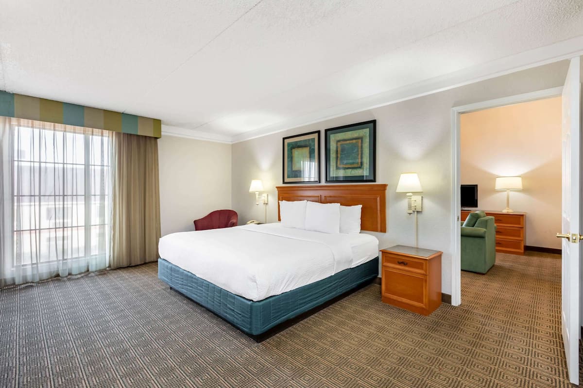 Habitación de hotel con una cama grande, un escritorio, una silla, un televisor y una puerta que da a otra habitación.