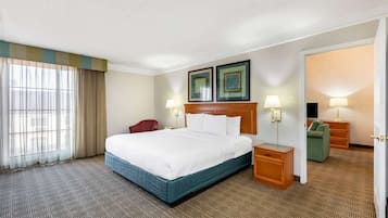 Habitación de hotel con una cama grande, un escritorio, una silla, un televisor y una puerta que da a otra habitación.