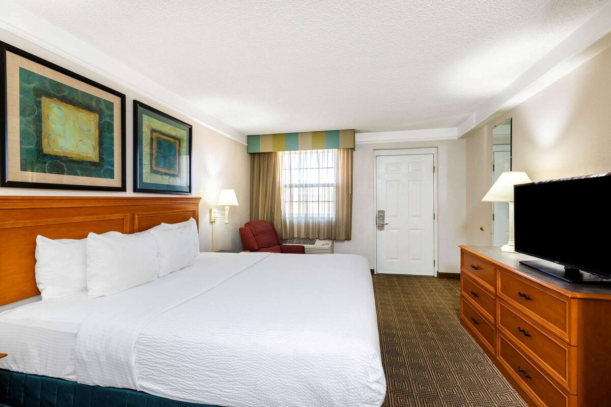 Una habitación de hotel con una cama grande, un televisor sobre un aparador de madera y dos cuadros en la pared.