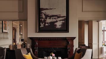 A room with a fireplace, a framed artwork, and a seating area with chairs and a table.