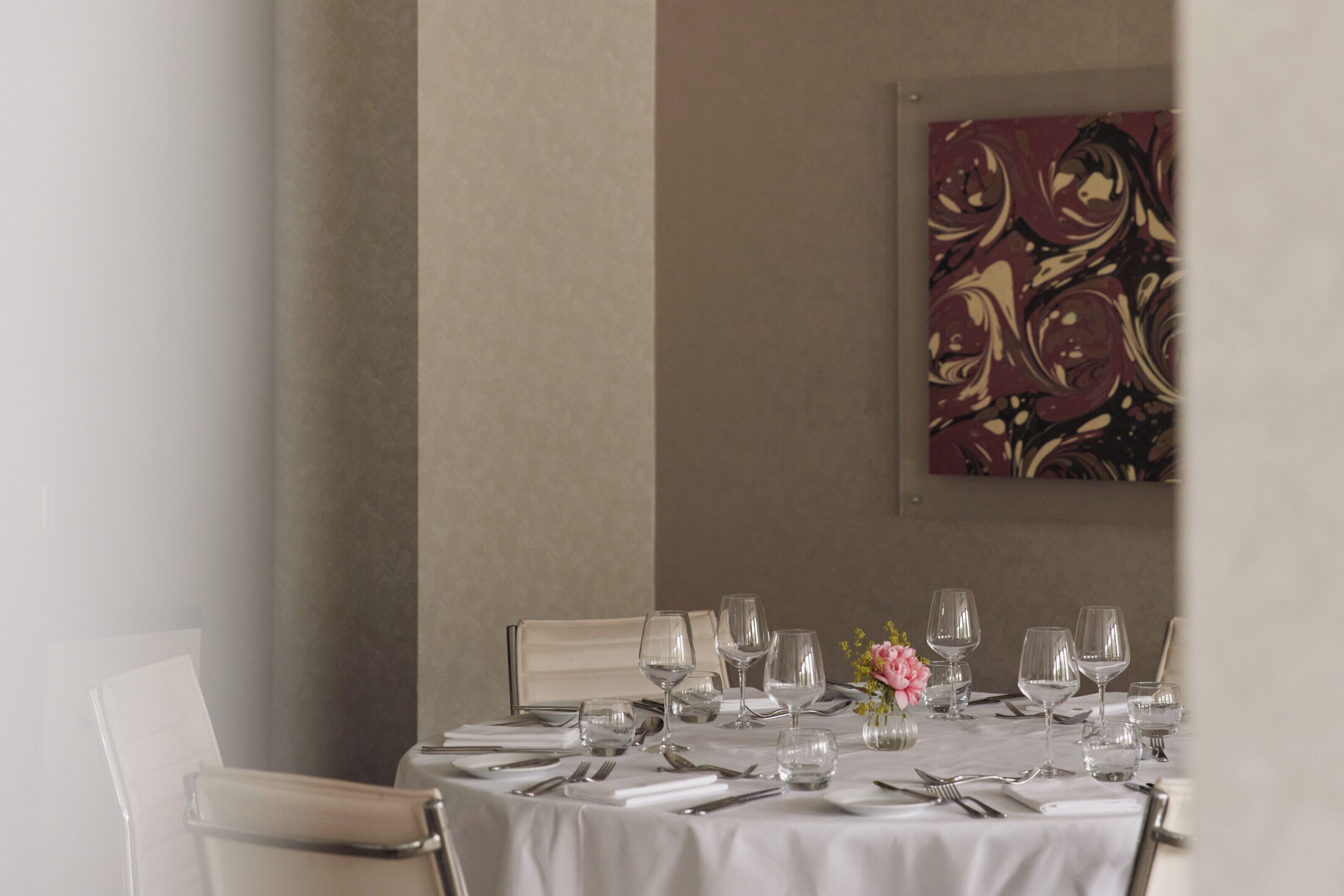 A dining table set with multiple wine glasses, cutlery, and a vase with flowers.
