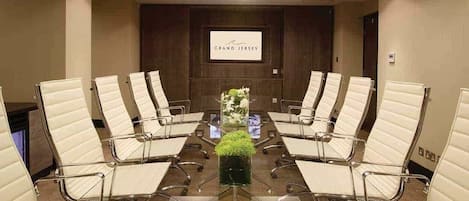 Un salón de conferencias con una larga mesa, sillas de cuero blanco y un logotipo en la pared.